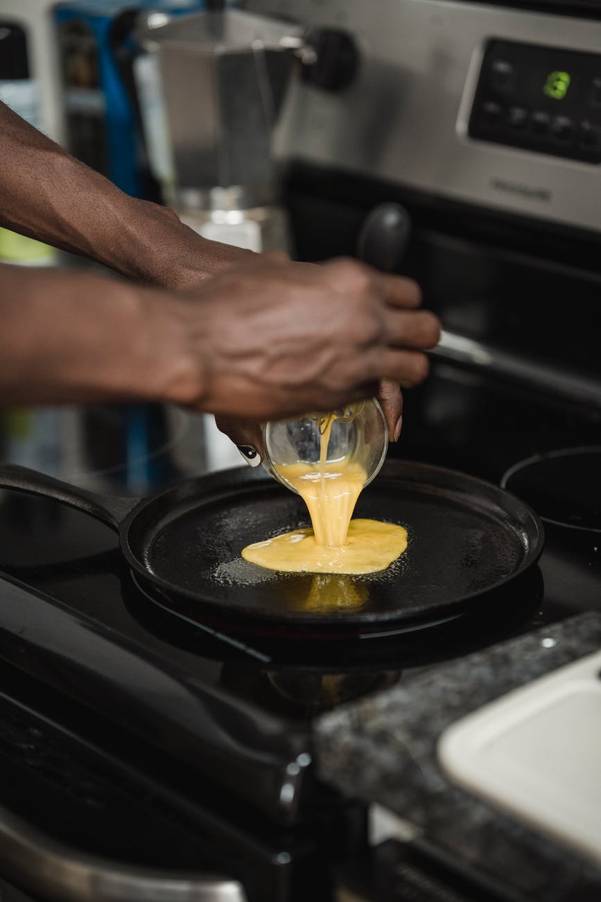 photo of a person pouring scrambled eggs on a black frying pan